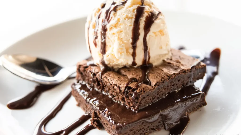 ice cream serving setup with a scoop of vanilla bean ice cream on top of fudgy chocolate brownie